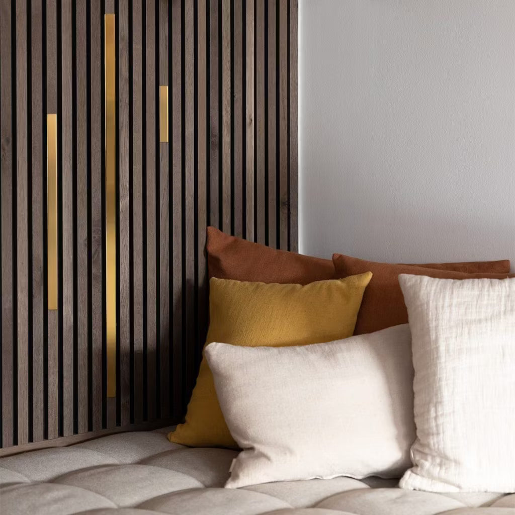 Des coussins crème, jaunes et bruns sur un canapé beige touffeté à côté dun panneau acoustique moderne avec des accents dorés pour un environnement confortable et contemporain.